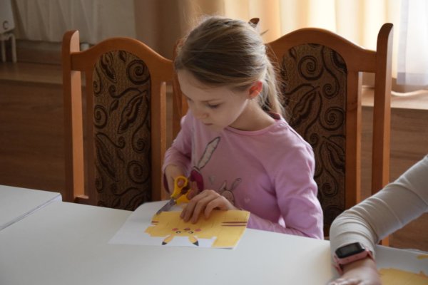 Zdjęcie przedstawia dziewczynkę wycinającą pokemona z papieru